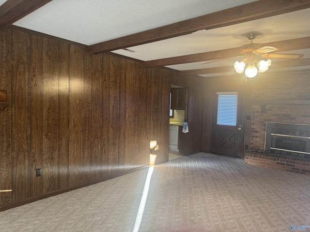 unfurnished living room with carpet flooring, ceiling fan, beamed ceiling, wood walls, and a fireplace