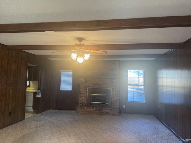 unfurnished living room with wooden walls, a fireplace, ceiling fan, and beamed ceiling