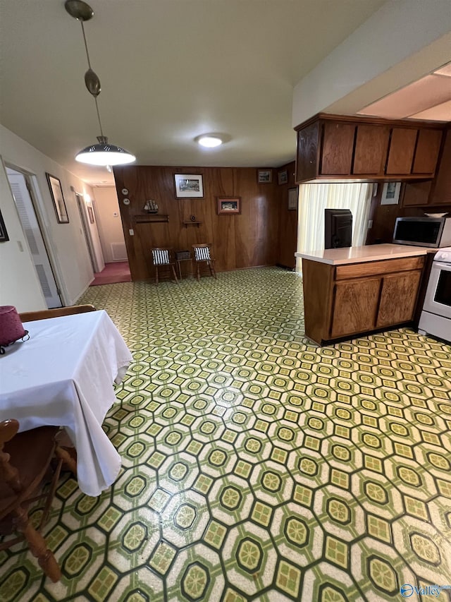 kitchen featuring kitchen peninsula, white electric stove, wood walls, and decorative light fixtures