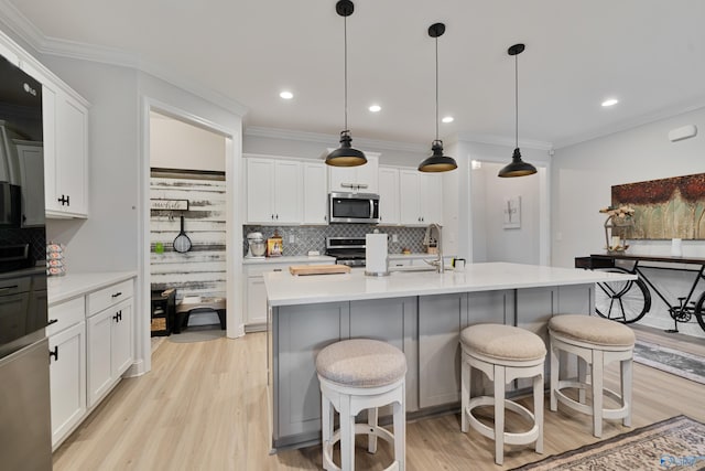 kitchen featuring backsplash, hanging light fixtures, an island with sink, a breakfast bar area, and stainless steel appliances