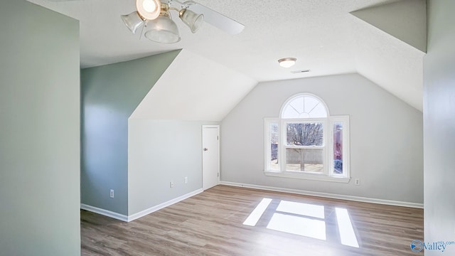 additional living space featuring lofted ceiling, light hardwood / wood-style flooring, and a textured ceiling