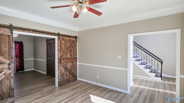 spare room with wood-type flooring, a barn door, ornamental molding, and ceiling fan