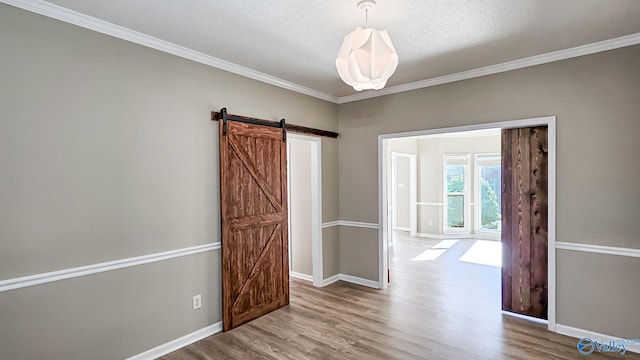 empty room with crown molding, a barn door, hardwood / wood-style floors, and a textured ceiling