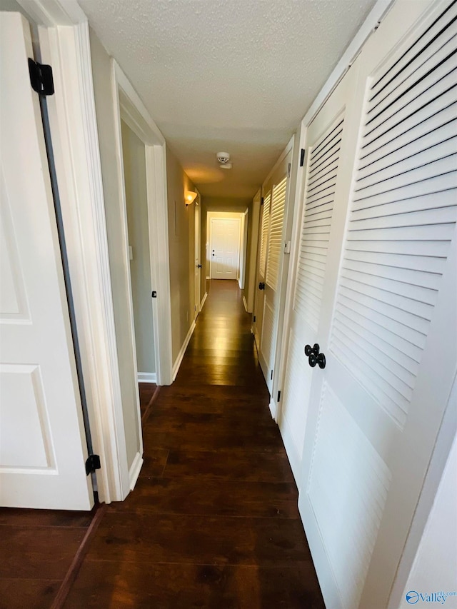 corridor with a textured ceiling and dark hardwood / wood-style floors