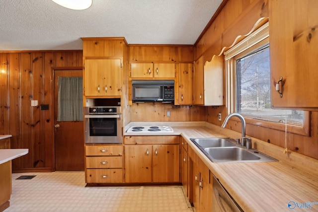 kitchen with light countertops, stainless steel oven, wood walls, a sink, and black microwave