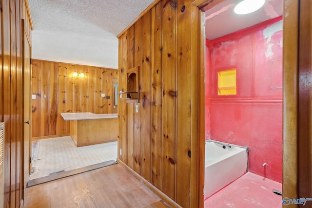 full bathroom with a textured ceiling, wooden walls, a bath, and wood finished floors