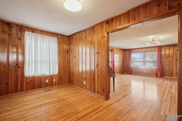 unfurnished room featuring visible vents, a textured ceiling, baseboards, and wood finished floors