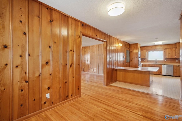 kitchen with light countertops, light wood-style flooring, a sink, dishwasher, and a peninsula