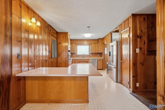 kitchen with stainless steel appliances, a peninsula, a sink, brown cabinets, and light floors