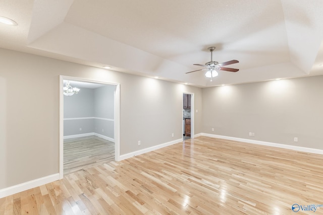 unfurnished room with ceiling fan with notable chandelier, light wood-type flooring, and a tray ceiling