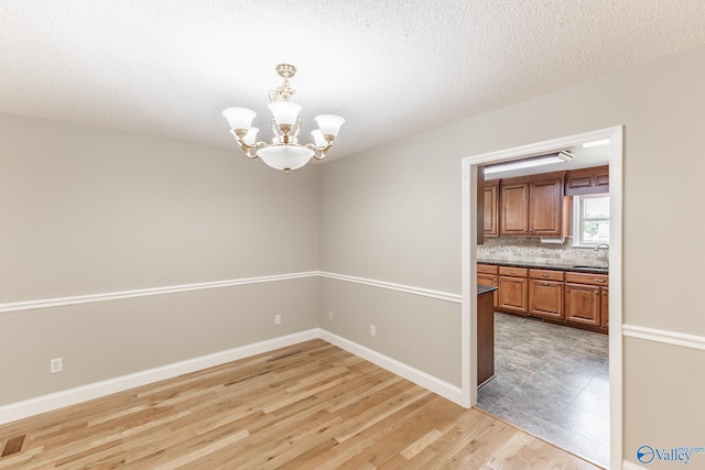 tiled empty room featuring sink, an inviting chandelier, and a textured ceiling