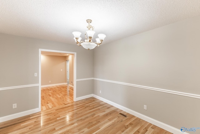 unfurnished room featuring a textured ceiling, hardwood / wood-style floors, and an inviting chandelier