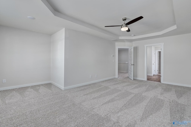 unfurnished bedroom with ceiling fan, a raised ceiling, and light carpet