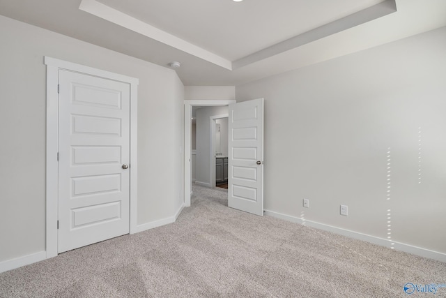 unfurnished bedroom with light colored carpet and a tray ceiling