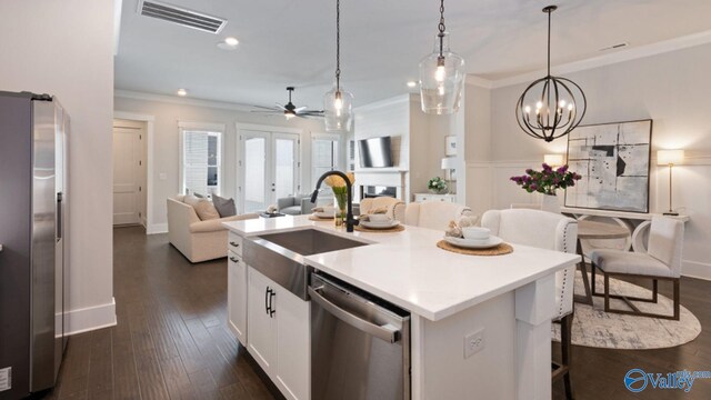 kitchen with dark hardwood / wood-style floors, ceiling fan with notable chandelier, a center island with sink, stainless steel appliances, and white cabinets