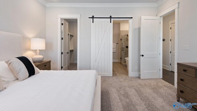 bedroom with a barn door, crown molding, light carpet, and ensuite bath