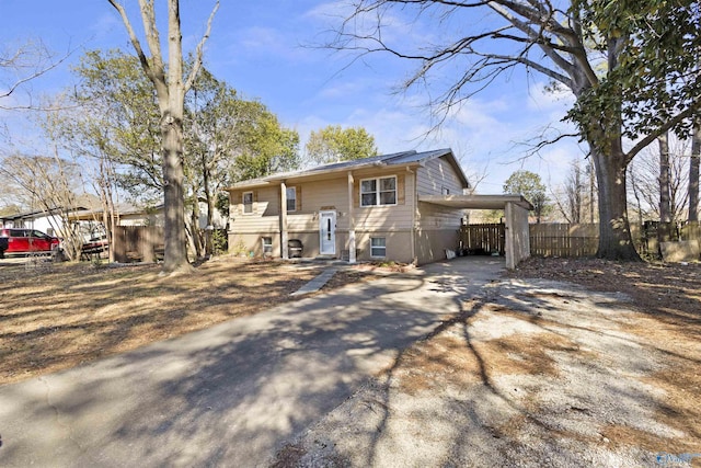 raised ranch featuring a carport, concrete driveway, and fence