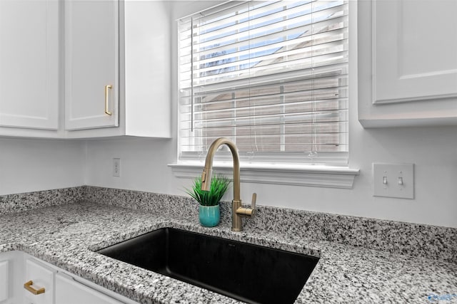 interior details featuring a sink, light stone counters, and white cabinets