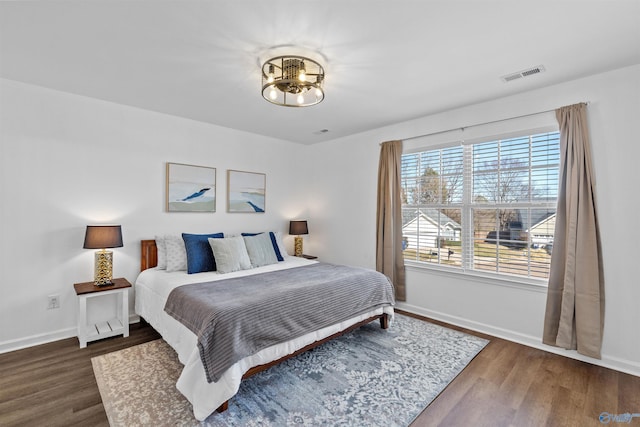 bedroom featuring a notable chandelier, visible vents, baseboards, and wood finished floors