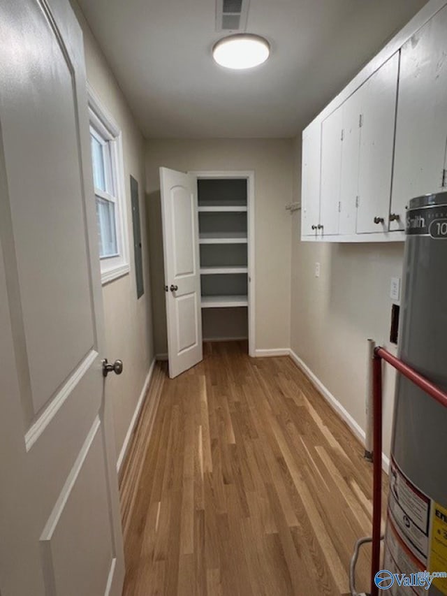 laundry area with visible vents, light wood finished floors, baseboards, water heater, and cabinet space