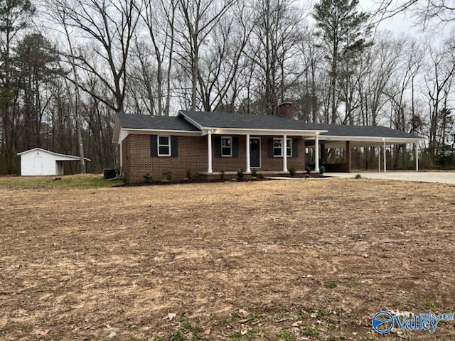 view of front of property featuring covered porch, a chimney, an outbuilding, brick siding, and a carport