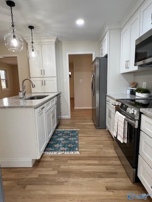 kitchen featuring a sink, white cabinetry, hanging light fixtures, stainless steel appliances, and light wood-style floors