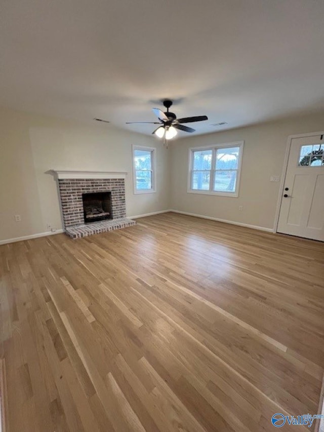 unfurnished living room featuring baseboards, light wood-style flooring, ceiling fan, and a brick fireplace