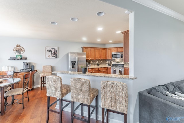 kitchen featuring stainless steel appliances, backsplash, kitchen peninsula, a kitchen bar, and hardwood / wood-style flooring