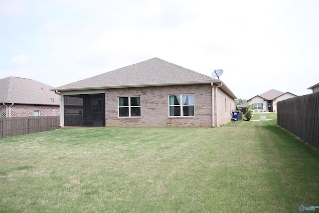 back of house featuring a lawn, a fenced backyard, a sunroom, and brick siding