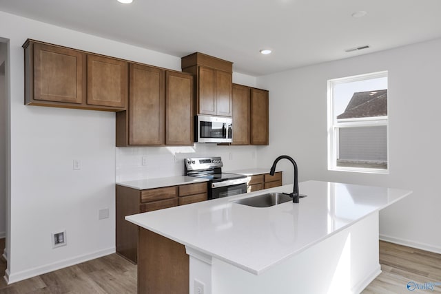 kitchen featuring appliances with stainless steel finishes, tasteful backsplash, an island with sink, sink, and light hardwood / wood-style flooring