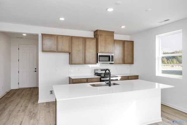 kitchen featuring appliances with stainless steel finishes, sink, decorative backsplash, a center island with sink, and light wood-type flooring