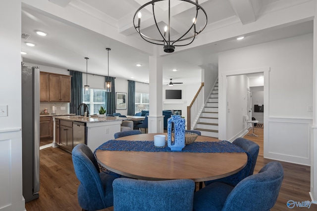 dining room with dark wood-style flooring, beam ceiling, ceiling fan with notable chandelier, wainscoting, and stairs