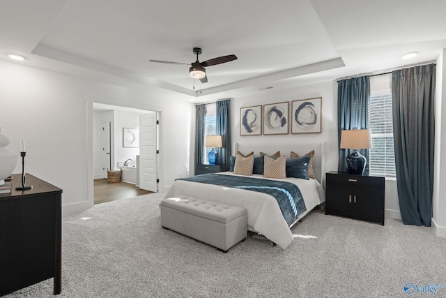 bedroom featuring connected bathroom, carpet floors, a ceiling fan, baseboards, and a tray ceiling