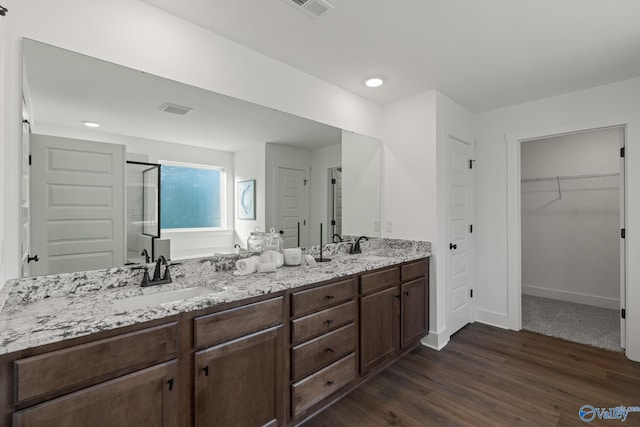 bathroom with double vanity, wood finished floors, a spacious closet, a shower stall, and a sink