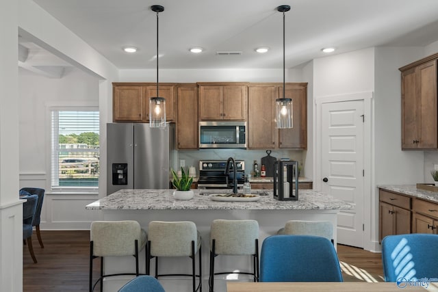 kitchen with dark wood-style floors, appliances with stainless steel finishes, a breakfast bar area, and decorative light fixtures