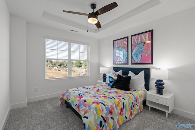 carpeted bedroom with ceiling fan, visible vents, baseboards, and a raised ceiling