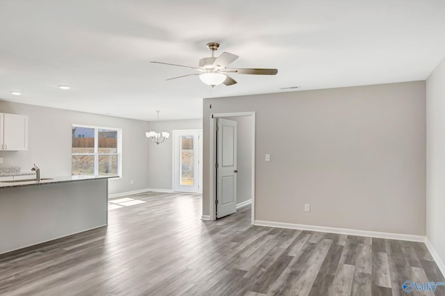 unfurnished living room featuring visible vents, baseboards, ceiling fan with notable chandelier, wood finished floors, and a sink