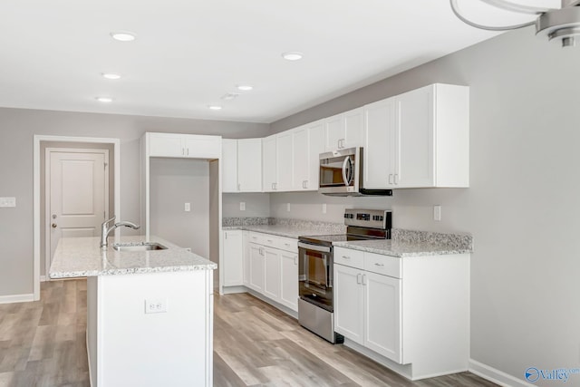 kitchen with light wood finished floors, appliances with stainless steel finishes, light stone countertops, and a sink