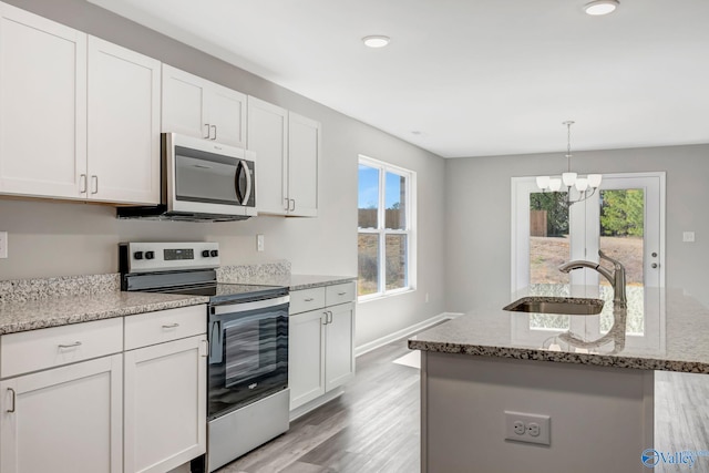 kitchen with light stone counters, a sink, light wood-style floors, appliances with stainless steel finishes, and white cabinetry