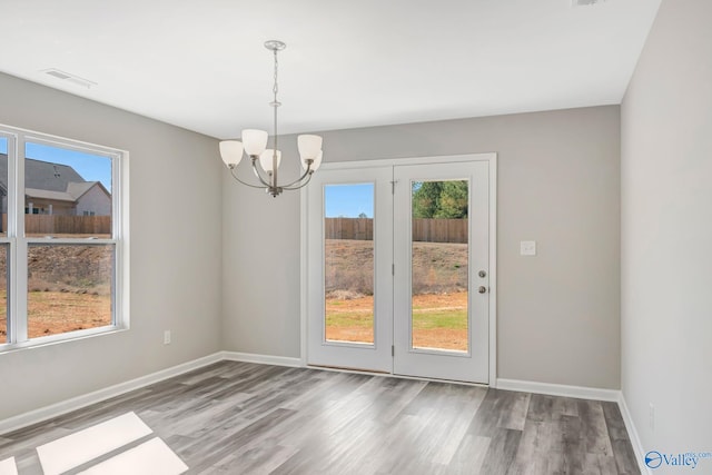 unfurnished dining area with wood finished floors, visible vents, a chandelier, and baseboards