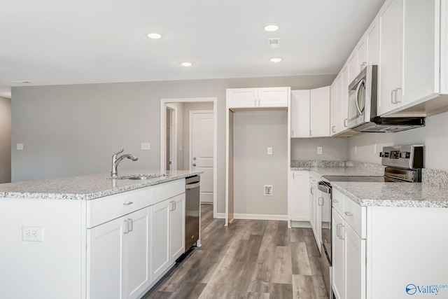 kitchen with light wood-type flooring, a center island with sink, a sink, stainless steel appliances, and white cabinets