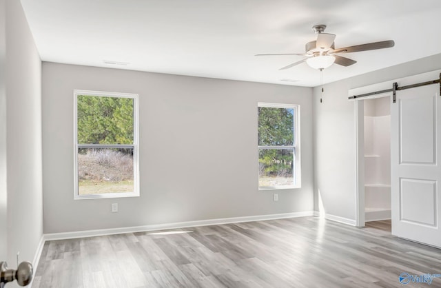 unfurnished bedroom featuring a barn door, light wood-style floors, baseboards, and ceiling fan