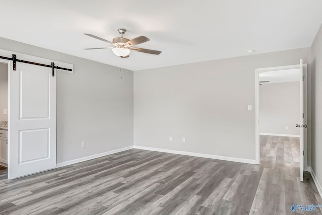 unfurnished bedroom with a barn door, baseboards, wood finished floors, and a ceiling fan