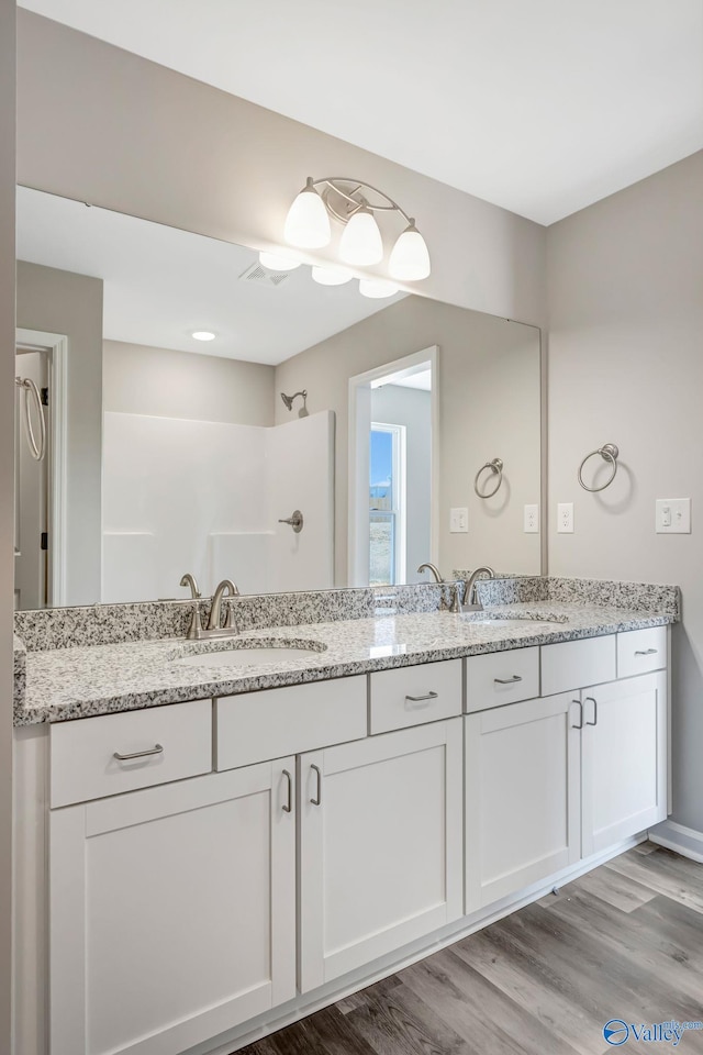 bathroom featuring a sink, a shower, wood finished floors, and double vanity