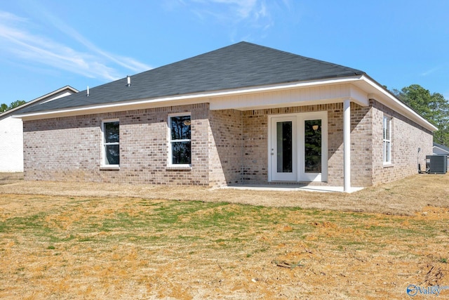 rear view of property featuring central air condition unit, brick siding, roof with shingles, and a yard