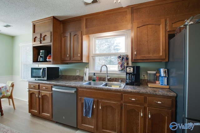 kitchen featuring stainless steel appliances, sink, a textured ceiling, and light hardwood / wood-style floors