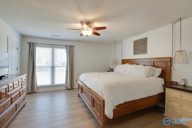 bedroom with a textured ceiling, ceiling fan, and light hardwood / wood-style floors