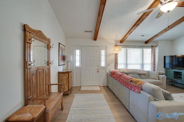 living room featuring beamed ceiling, ceiling fan, a textured ceiling, and light wood-type flooring