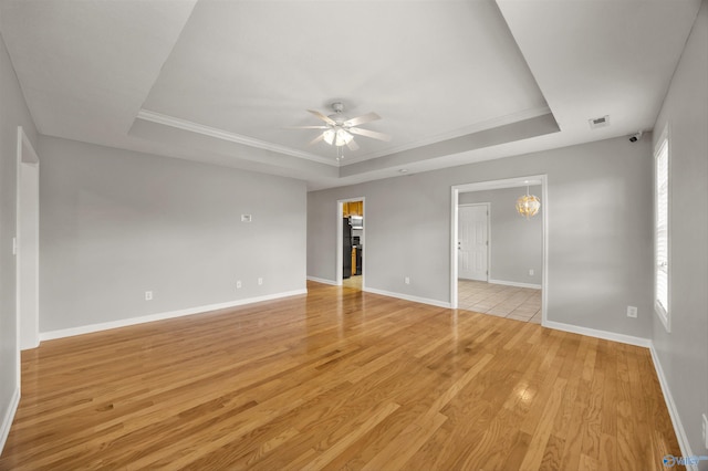 unfurnished bedroom with a raised ceiling, ceiling fan with notable chandelier, light hardwood / wood-style flooring, and a walk in closet