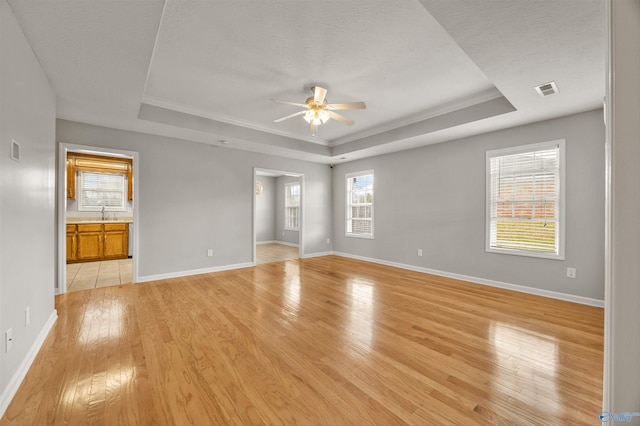 interior space featuring light wood-type flooring, crown molding, a textured ceiling, a tray ceiling, and ceiling fan